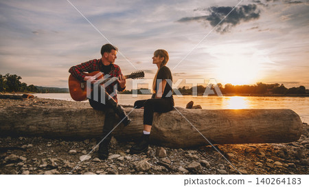 Friends Playing Acoustic Guitar by River at Sunset Friends Playing Acoustic Guitar by River at Sunset 140264183
