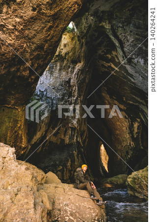 Hiker Resting inside Large Cave during Outdoor Adventure Hiker Resting inside Large Cave during Outdoor Adventure 140264241