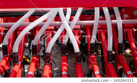 Detailed view of a red farm machine with white corrugated hoses, metal tubes, bolts, and numbered parts arranged in a dense mechanical assembly under bright daylight Detailed view of a red farm machine with white corrugated hoses, metal tubes, bolts, and numbered parts arranged in a dense mechanical assembly under bright daylight 140264311