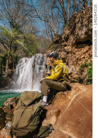 Hiker Resting Near Waterfall During Trekking Adventure Hiker Resting Near Waterfall During Trekking Adventure 140264316