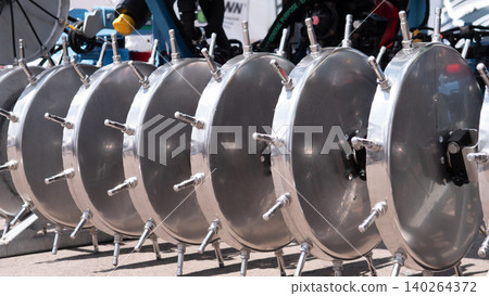 Row of large stainless steel industrial vessels with bolted circular covers arranged outdoors at a facility, with workers and machinery blurred in the background Row of large stainless steel industrial vessels with bolted circular covers arranged outdoors at a facility, with workers and machinery blurred in the background 140264372