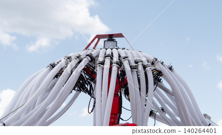 Red industrial equipment fitted with numerous flexible white hoses and cables is shown from a low angle against a bright blue sky with clouds, creating a technical outdoor Red industrial equipment fitted with numerous flexible white hoses and cables is shown from a low angle against a bright blue sky with clouds, creating a technical outdoor 140264401