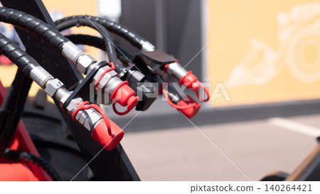 Closeup of black hydraulic hoses with metal fittings and red protective caps attached to industrial equipment, with a blurred yellow background and soft indoor lighting Closeup of black hydraulic hoses with metal fittings and red protective caps attached to industrial equipment, with a blurred yellow background and soft indoor lighting 140264421