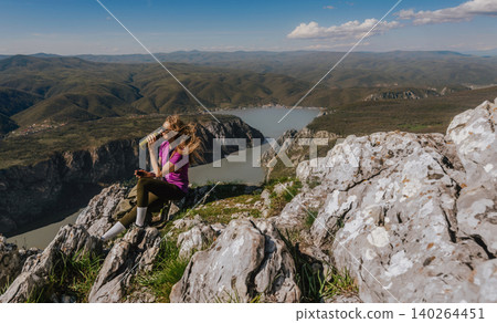 Woman Hiker Sitting on Mountain Peak Drinking Water Woman Hiker Sitting on Mountain Peak Drinking Water 140264451