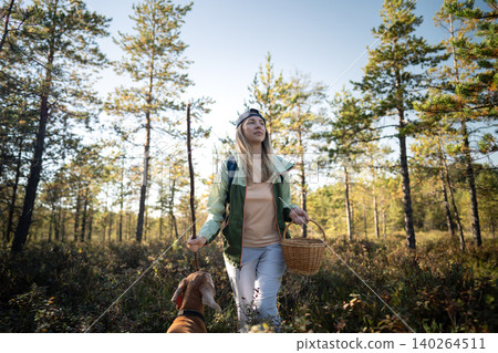 Active positive woman backpacker making way through swampy pine forest accompanied by Vizsla dog 140264511