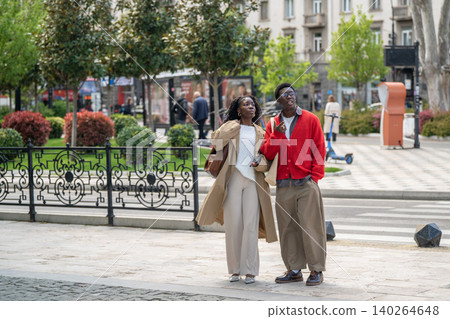 Smiling positive african american man and woman friends enjoying modern city area on daily walk Smiling positive african american man and woman friends enjoying modern city area on daily walk 140264648