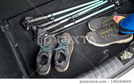 Hiking gear including trekking poles and two pairs of shoes arranged in the trunk of a vehicle, ready for outdoor adventure and exploration. High quality photo Hiking gear including trekking poles and two pairs of shoes arranged in the trunk of a vehicle, ready for outdoor adventure and exploration. High quality photo 140264649