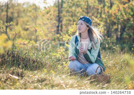 Tranquil positive woman forager sitting at forest bog collecting and eating wild marsh cranberries 140264738