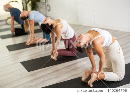 Young European woman practicing yoga, Camel position Ustrasana, indoor class with women, studio background Young European woman practicing yoga, Camel position Ustrasana, indoor class with women, studio background 140264796