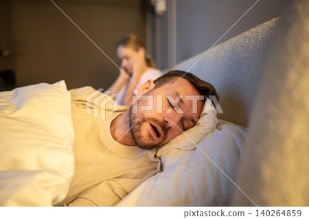 Married couple struggles and relationship stress, tired woman covering ears from noisy snoring sound Married couple struggles and relationship stress, tired woman covering ears from noisy snoring sound 140264859