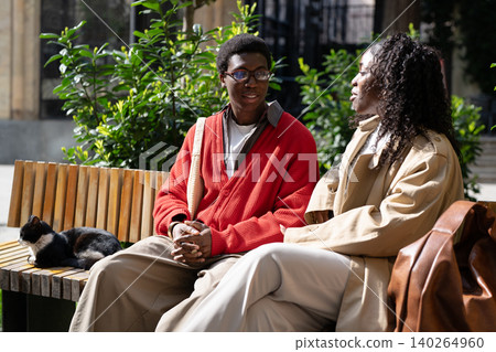 Relaxed african american couple man and woman sitting together on bench in park and talking 140264960