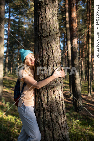 Loving nature purity. Relaxed woman hugging tree trunk in autumn forest with closed eyes at sunset. 140265011