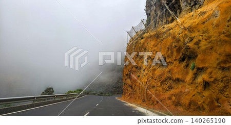 Winding asphalt road curves through mountainous terrain with yellow and orange rock formations and green pine trees under a cloudy sky in a scenic landscape. High quality photo Winding asphalt road curves through mountainous terrain with yellow and orange rock formations and green pine trees under a cloudy sky in a scenic landscape. High quality photo 140265190
