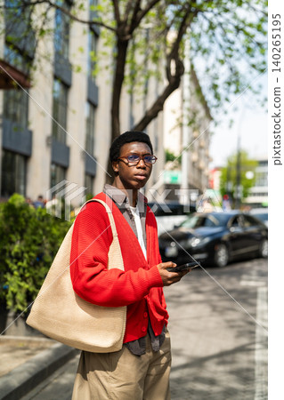 Focused african american man student holding smartphone in hand standing on street waiting for taxi. Focused african american man student holding smartphone in hand standing on street waiting for taxi. 140265195