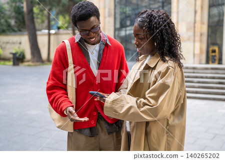 Cheerful smiling african american woman showing photos on smartphone to positive black male friend. Cheerful smiling african american woman showing photos on smartphone to positive black male friend. 140265202