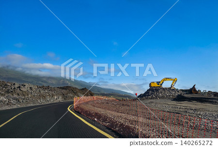 Specialized equipment machine with hydraulic arm positioned on volcanic rock and solidified lava overlooking the ocean under a clear blue sky with distant mountains visible. High quality photo Specialized equipment machine with hydraulic arm positioned on volcanic rock and solidified lava overlooking the ocean under a clear blue sky with distant mountains visible. High quality photo 140265272