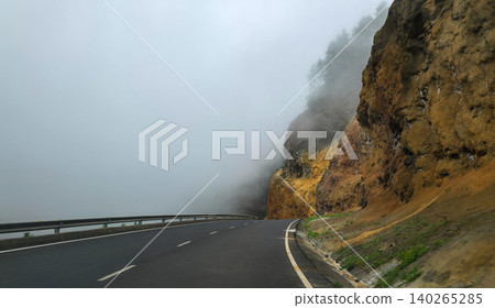 Winding asphalt road curves through mountainous terrain with yellow and orange rock formations and green pine trees under a cloudy sky in a scenic landscape. High quality photo Winding asphalt road curves through mountainous terrain with yellow and orange rock formations and green pine trees under a cloudy sky in a scenic landscape. High quality photo 140265285