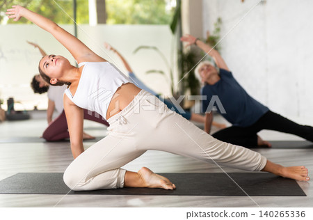Group of sporty women practicing various yoga positions during training indoors, focus on young female Group of sporty women practicing various yoga positions during training indoors, focus on young female 140265336