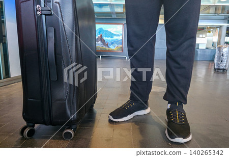 A man in comfortable sports clothes and shoes is standing near a suitcase, heading on a trip. High quality photo A man in comfortable sports clothes and shoes is standing near a suitcase, heading on a trip. High quality photo 140265342