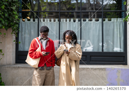Thoughtful african american man and woman friends standing on street browsing online on smartphones. Thoughtful african american man and woman friends standing on street browsing online on smartphones. 140265370