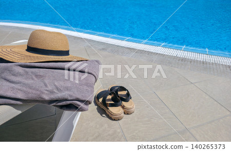 Sun hat, towel, and sandals arranged on a lounge chair beside a pool. Items for beach recreation. High quality photo Sun hat, towel, and sandals arranged on a lounge chair beside a pool. Items for beach recreation. High quality photo 140265373