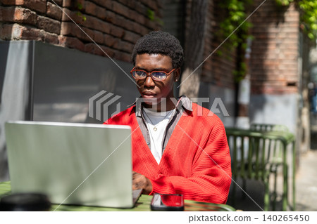 Concentrated positive african american man student working on laptop outside in street cafe in city. Concentrated positive african american man student working on laptop outside in street cafe in city. 140265450