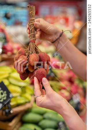 Woman choosing ripe lychee fruits at supermarket in Thailand, holding bunch of fruits on branches. Woman choosing ripe lychee fruits at supermarket in Thailand, holding bunch of fruits on branches. 140265552