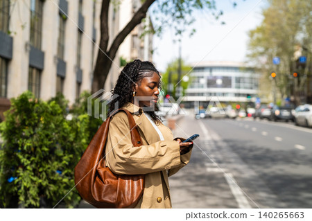 Serious african american woman on street waiting for public transport and checks schedule on phone. Serious african american woman on street waiting for public transport and checks schedule on phone. 140265663