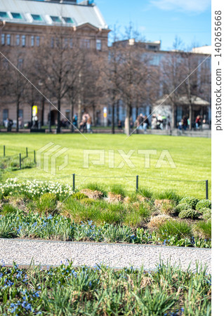 Young well-groomed grass lawn with neat flowerbeds and spring flowers arranged in public garden. Young well-groomed grass lawn with neat flowerbeds and spring flowers arranged in public garden. 140265668