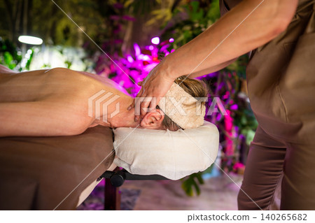 Woman lying on spa bed in salon receiving relaxation massage treatment from professional masseur. Woman lying on spa bed in salon receiving relaxation massage treatment from professional masseur. 140265682