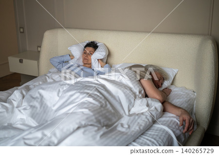 Elderly husband sleeping and snoring loudly at night causing discomfort and frustration to wife. 140265729