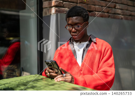 Focused african american man relaxing on outdoor terrace in city cafe scrolling media on smartphone. Focused african american man relaxing on outdoor terrace in city cafe scrolling media on smartphone. 140265733