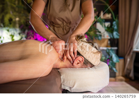 Woman lying on spa bed in salon receiving relaxation massage treatment from professional masseur. Woman lying on spa bed in salon receiving relaxation massage treatment from professional masseur. 140265759