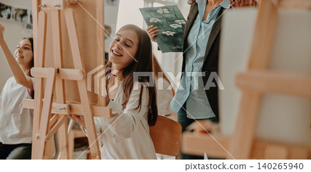 Happy Caucasian teen girl painting on easel during creative class in bright art school studio 140265940