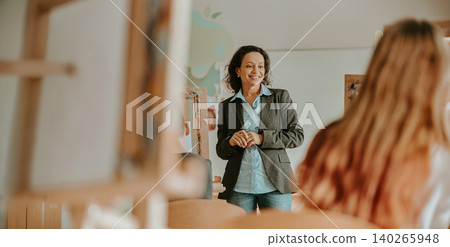 Happy mid adult Hispanic female art teacher instructing students in a bright classroom studio Happy mid adult Hispanic female art teacher instructing students in a bright classroom studio 140265948