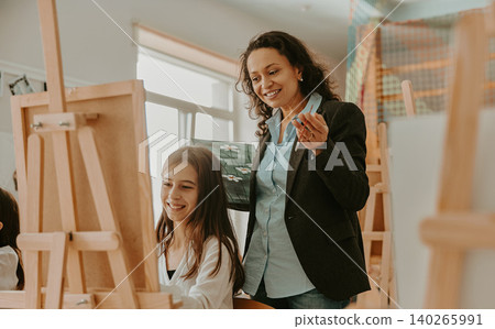 Hispanic adult woman teaching a young Caucasian girl how to paint in a bright art studio Hispanic adult woman teaching a young Caucasian girl how to paint in a bright art studio 140265991