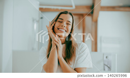 Happy young adult Caucasian woman smiling and touching her face in a bright modern bathroom Happy young adult Caucasian woman smiling and touching her face in a bright modern bathroom 140265996