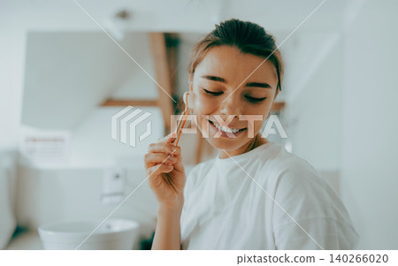 Happy young adult Caucasian woman massaging her face with a roller in a bright bathroom Happy young adult Caucasian woman massaging her face with a roller in a bright bathroom 140266020