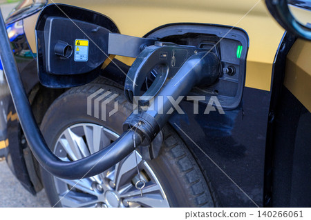 Electric car charging process close up view, EV black connector plugged into vehicle socket at public station Electric car charging process close up view, EV black connector plugged into vehicle socket at public station 140266061