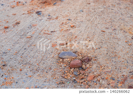 Small stones and orange clay fragments on sandy road surface, close-up texture of rural dirt pathway ground Small stones and orange clay fragments on sandy road surface, close-up texture of rural dirt pathway ground 140266062