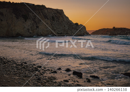rocky pebble beach foreground with soft ocean waves approaching massive cliffs during golden hour rocky pebble beach foreground with soft ocean waves approaching massive cliffs during golden hour 140266138