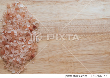 Coarse Himalayan pink salt crystals scattered on a natural wood surface. Tactile organic composition with warm timber grain, coral mineral tones, and copy space 140266143