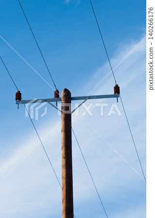 Close up of a weathered timber utility pole featuring brown ceramic insulators and steel crossarm. Detailed industrial texture of aged wood against a clear blue sky Close up of a weathered timber utility pole featuring brown ceramic insulators and steel crossarm. Detailed industrial texture of aged wood against a clear blue sky 140266176