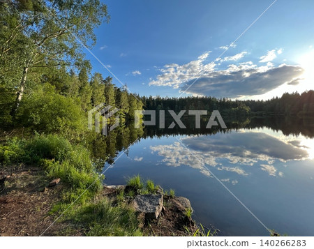 Scenic lake view with reflections of trees and clouds in the water Scenic lake view with reflections of trees and clouds in the water 140266283
