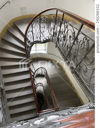 Elegant spiral staircase with ornate railing and natural light from window Elegant spiral staircase with ornate railing and natural light from window 140266332