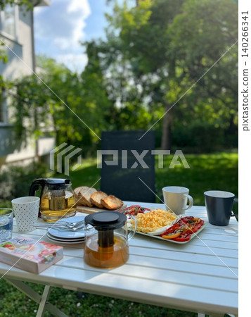 Breakfast table setting with tea, bread, and vegetables in garden Breakfast table setting with tea, bread, and vegetables in garden 140266341