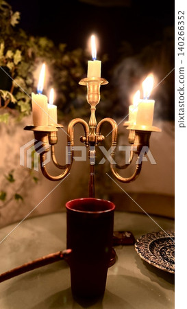 Candlelit brass candelabra with four candles on glass table setting 140266352