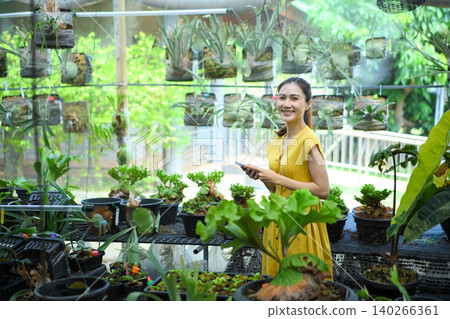 Smiling woman in greenhouse surrounded by plants, expressing calm, nature connection, and lifestyle Smiling woman in greenhouse surrounded by plants, expressing calm, nature connection, and lifestyle 140266361