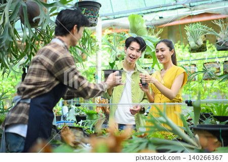 Gardener handing plant to happy in nursery Gardener handing plant to happy in nursery 140266367