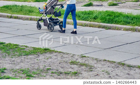 Legs in jeans of young mother walking with baby stroller Legs in jeans of young mother walking with baby stroller 140266443